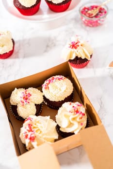 Packaging freshly baked red velvet cupcakes with white chocolate ganache frosting into the cupcake box.