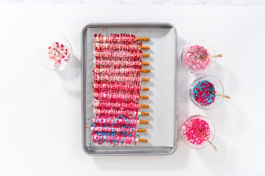 Flat lay. Drizzling melted chocolate over chocolate-dipped pretzels rods and decorating with sprinkles to make chocolate-covered pretzel rods for Valentine's Day.