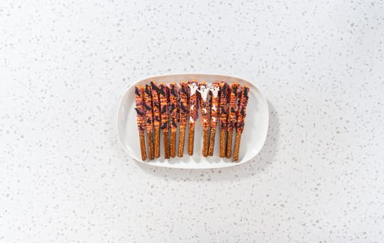 Flat lay. Halloween chocolate-covered pretzel rods with sprinkles on a white serving plate.