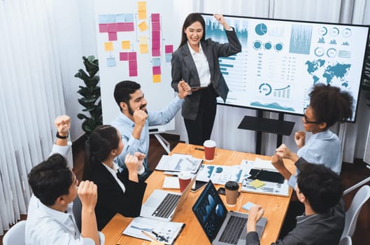 Business people celebrate after successful presentation or meeting on data analysis display on TV screen. Happy team gathers in office room, cheer to collaboration with celebratory gesture. Concord