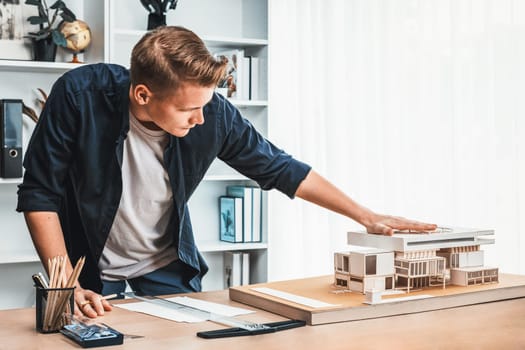 Architect designer studies elegant house model, reviewing structure design for improvement with construction plan on table. Creativity and innovation in architectural design. Iteration