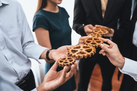 Office worker holding cog wheel as unity and teamwork in corporate workplace concept. Diverse colleague business people showing symbol of visionary system and mechanism for business success. Concord