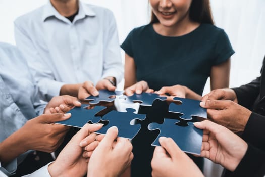 Diverse corporate officer workers collaborate in office, connecting puzzle pieces to represent partnership and teamwork. Unity and synergy in business concept by merging jigsaw puzzle. Concord