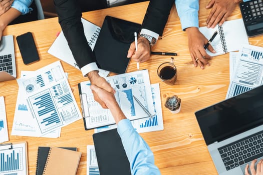 Two businessman shake hand in meeting room with coworker give cheerful applause. Team of analyst celebrate after successful significant progress on business strategic performance. Meticulous