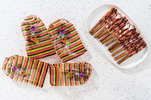 Flat lay. Packaging Halloween chocolate-covered pretzel rods with sprinkles into gift bags.