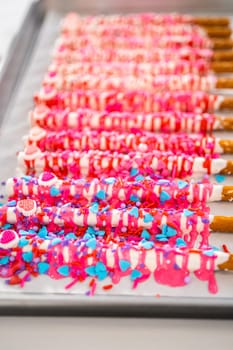 Drizzling melted chocolate over chocolate-dipped pretzels rods and decorating with sprinkles to make chocolate-covered pretzel rods for Valentine's Day.