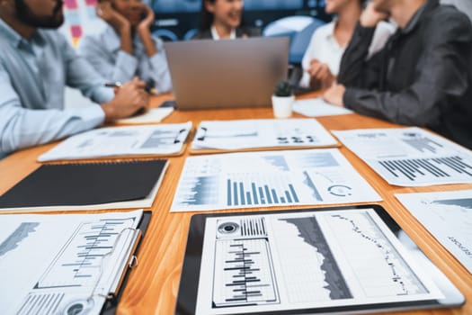 Focus financial dashboard paper showing graphs and chart with blurred background of diverse business people analyzing business data by BI Fintech technology for business marketing indication. Concord