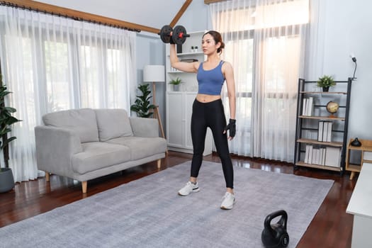 Vigorous energetic woman doing dumbbell weight lifting exercise at home. Young athletic asian woman strength and endurance training session as home workout routine.