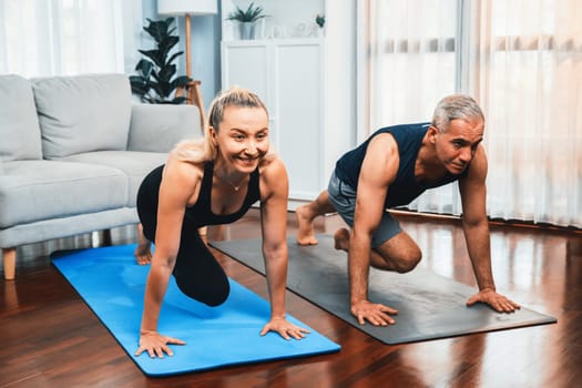 Athletic and active senior couple doing exercise on fit mat with plank climbing together at home exercise as concept of healthy fit body lifestyle after retirement. Clout