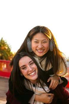 Playful smiling multiracial female couple looking at camera. Woman piggyback ride with girlfriend. Vertical image. LGBT concept.