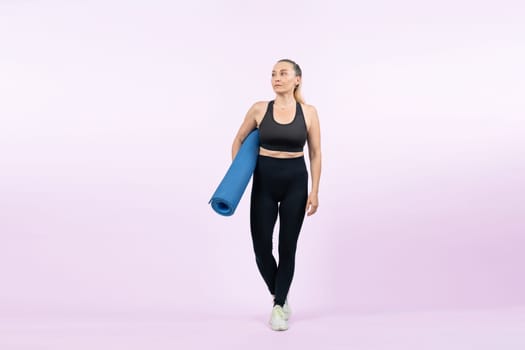 Full body length shot athletic and sporty senior woman holding fitness exercising mat on isolated background. Healthy active physique and body care lifestyle after retirement. Clout