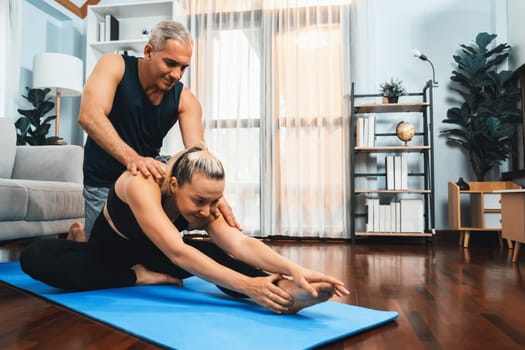 Happy active senior couple in sportswear being supportive and assist on yoga posture together at home. Healthy senior man and woman lifestyle with yoga exercise. Clout