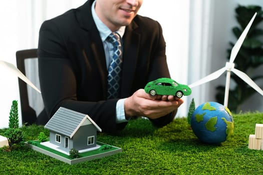 Eco business and save Earth concept shown by businessman or CEO holding paper globe in office with eco friendly mockup to promote CO2 and carbon footprint reduction for greener future. Quaint