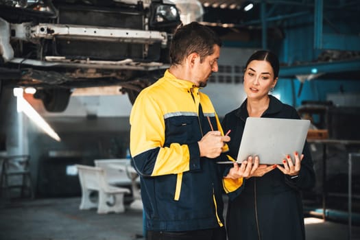 Two vehicle mechanic working together, conduct car inspection with laptop. Automotive service technician in uniform carefully make diagnostic troubleshooting to identify error. oxus