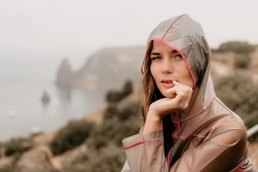 Woman rain park. Happy woman portrait wearing a raincoat with transparent umbrella outdoors on rainy day in park near sea. Girl on the nature on rainy overcast day