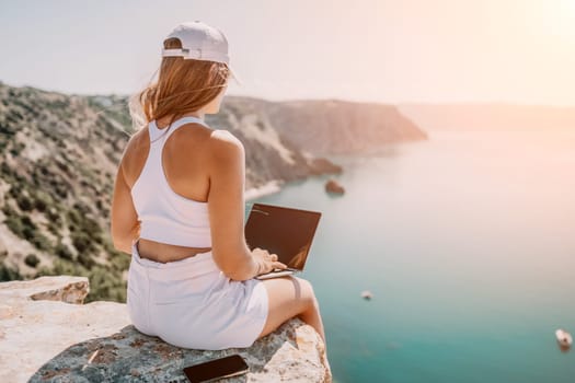 Digital nomad, Business woman working on laptop by the sea. Pretty lady typing on computer by the sea at sunset, makes a business transaction online from a distance. Freelance remote work on vacation