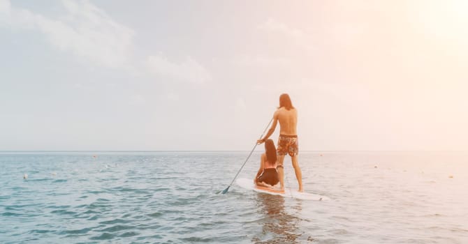 Sea woman and man on sup. Silhouette of happy young woman and man, surfing on SUP board, confident paddling through water surface. Idyllic sunset. Active lifestyle at sea or river
