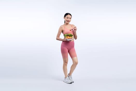 Young sporty Asian woman in sportswear holding salad bowl fill with vibrant of fruit and vegetable. Natural youthful and fit body lifestyle with balance nutrition on isolated background. Vigorous