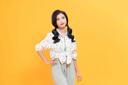 Close up portrait of young attractive smiling girl with pigtails standing isolated over yellow background