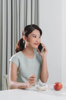 Attractive smiling young woman having a healthy breakfast and talking on mobile phone