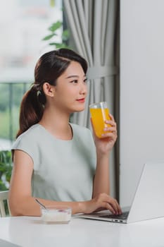 Satisfied woman drinking orange juice using a laptop on a desk at home