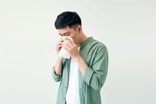 Young man wiping his nose with a tissue on white background