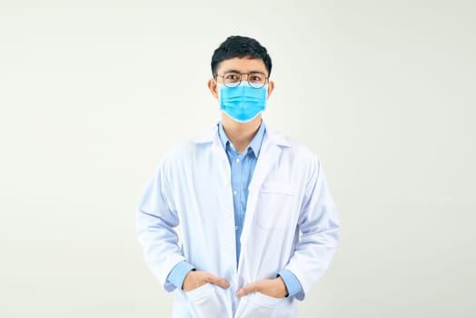 young doctor in medical mask standing with crossed arms and looking at camera isolated on white