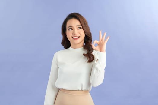 Portrait of happy Asian woman shows ok sign and looking at the camera on color background.