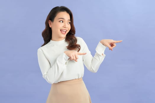 Asian young woman makes gesture two fingers pointed sideways above presenting product something