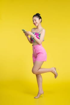 Beautiful Asian woman holding smartphone and smiling on light yellow background