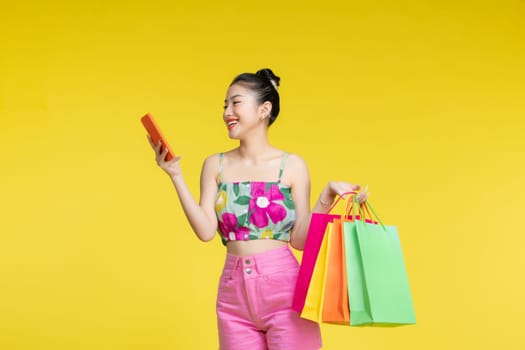 Young energetic Asian woman holding blank use smartphone searching shop retail with colorful shopping bags 