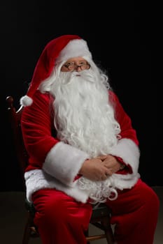 Santa Claus sits on a black background and looks at the camera. Christmas, New Year, Holiday Celebration, space for text