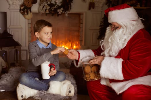 Santa Claus treats a boy with oatmeal cookies against the background of a fireplace and a Christmas tree, New Year's holiday, Christmas