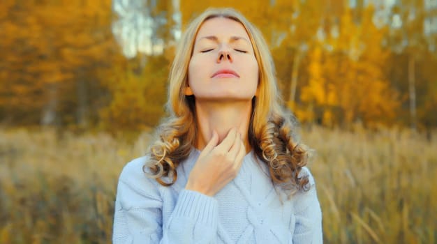 Sick exhausted young woman suffering from acute sore in throat flu, touches her neck with hand, she feels bad outdoors in autumn park, fall season