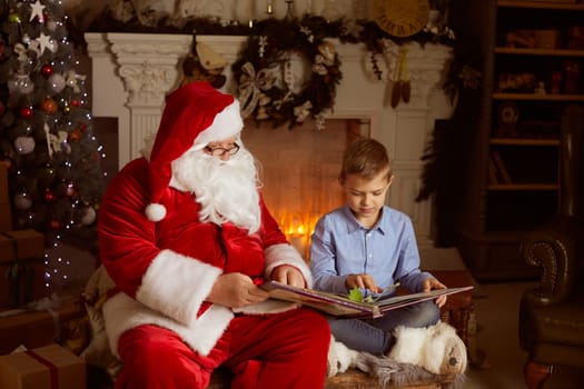 Santa Claus and a boy reading a book against the background of a fireplace and a Christmas tree, New Year's holiday, Christmas