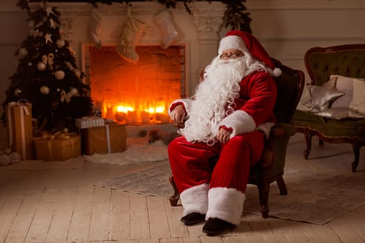 Santa Claus sits in a cozy chair by the fireplace with a Christmas tree, surrounded by Christmas decorations and gifts.