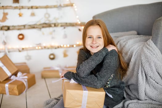 little girl holding craft gift against background of christmas tree with wooden new year toys hanging on wall