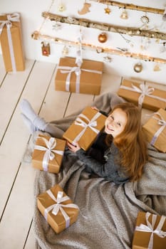 little girl holding craft gift against background of christmas tree with wooden new year toys hanging on wall, vertical photo