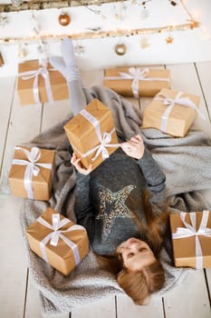 little girl holding craft gift against background of christmas tree with wooden new year toys hanging on wall, vertical photo