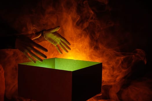 human hands taking out surprise from mysterious box on dark red background surrounded by smoke, mystery box