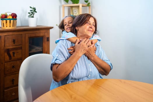 Happy loving girl embraces her grandmother from behind at home, sharing joyful and affectionate moment that radiates warmth and connection in their cozy living space