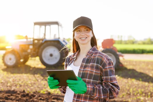 a girl agronomist with a tablet manages agribusiness against the background of a tractor, modern agribusiness