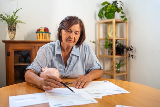 Focused senior woman carefully reviews financial bills on table at home, concentrating as she manages her finances in quiet and thoughtful moment