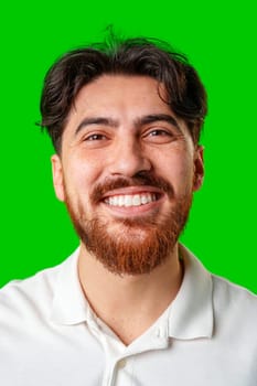 A smiling young man with a beard poses against a bright green background close up