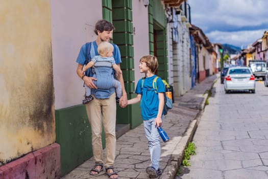 Father and and his two sons, a teenager and a baby tourists walks through the colonial streets San Cristobal de las Casas, Mexico. Cultural exploration, architecture, and travel experience concept.