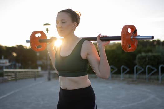 Sportswoman is lifting weights during an outdoor training at sunset
