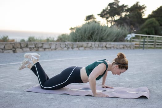 Young sporty woman is working out outdoor, doing push-ups on a mat