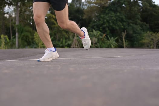 Low angle shot sportsman legs in sport shoes jogging along a paved road. Fitness and active lifestyle.