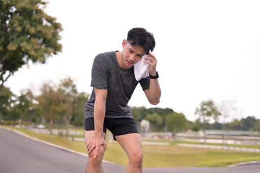 Tired young sportsman taking a break from exercising wiping sweat from his face with a white towel.