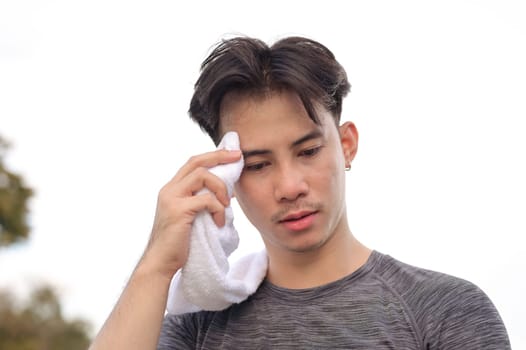 Tired young sportsman taking a break from exercising wiping sweat from his face with a white towel.